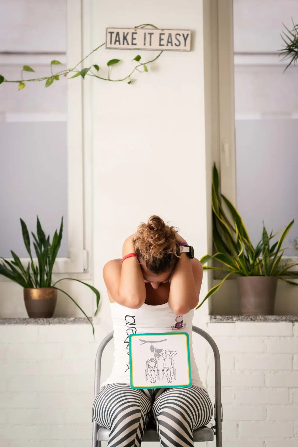 Monika sitzt auf einem Stuhl mit hinter ihrem Kopf verschränkten Armen, die Ellenbogen sind nach vorne gerichtet